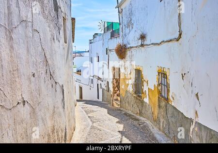 Die schmale geschwungene Straße von Pueblo Blanco (weiße Stadt) mit mittelalterlichen schäbigen Häusern, leere Wände mit zerbröckeltem Putz, Arcos, Spanien Stockfoto