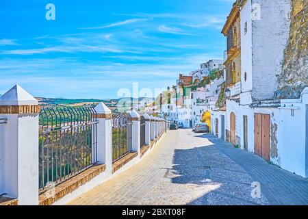 Die alte Straße verläuft am steilen Hang des Stadthügels entlang und eröffnet den Blick auf weiße Wohnviertel und Berglandschaften in Arcos Umgebung, Stockfoto