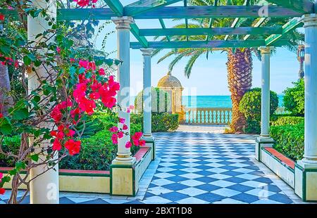 Die hohen Säulen und das Holzdach des Vintage-Pavillons im Paseo de Carlos III Garten, mit blühenden Büschen von Bougainvillea und topiary pl Stockfoto