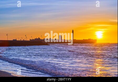 Genießen Sie den Sonnenuntergang über dem Atlantischen Ozean mit Blick auf die Flutwellen und die Silhouette der mittelalterlichen Burg San Sebastian mit dem hohen Leuchtturm, Cadiz, Spanien Stockfoto