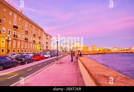 CADIZ, SPANIEN - 23. SEPTEMBER 2019: Gehen Sie auf dem Paseo del Vendaval spazieren und sehen Sie die mittelalterliche Kathedrale von Cadiz, die Küste des Atlantischen Ozeans und den violetten Abendhimmel am September Stockfoto