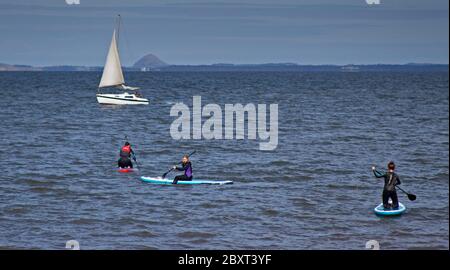 Portobello, Edinburgh, Schottland, Großbritannien. Juni 2020. An diesem Nachmittag war nicht viel los auf der Promenade oder am Strand, die Temperatur lag bei 16 Grad, aber die Brise war kühl. Ein kleines Segelboot und drei weibliche Paddle boardern auf dem Firth of Forth sowie einige Schwimmer. Stockfoto