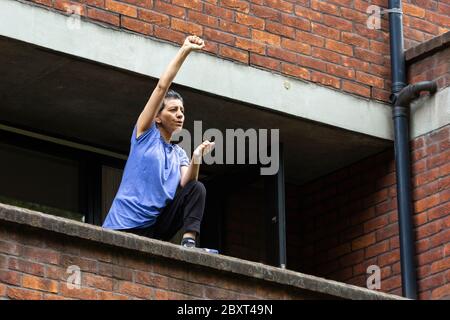 Eine Frau steht auf einem Balkon und hebt ihre Faust zur Unterstützung des Black Lives Matters Protests auf der Vauxhall Bridge Road, London, 6. Juni 2020 Stockfoto