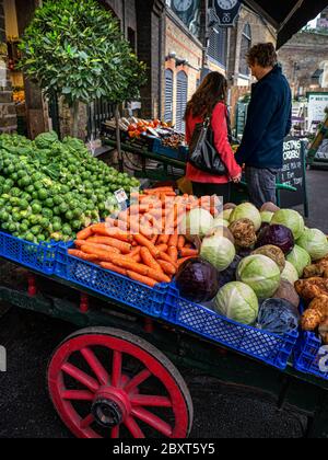 BOROUGH MARKET GEMÜSE paar Browsing Auswahl an frischem britischem Gemüse einschließlich Rosenkohl, Karotten, Kohlraben, Kartoffeln, auf dem Verkauf auf traditionellen Markt Barren in Borough Market Southwark London UK Stockfoto