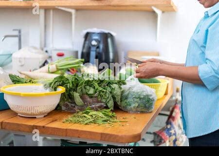 Asiatische Frau hält Messer und bereitet viel Gemüse für das Kochen in der hinteren Küche. Stockfoto