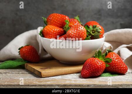 Erdbeerkonzept mit einer Gruppe reifer roter Erdbeeren in einer weißen Schale Nahaufnahme Frontansicht auf einem rustikalen Holztisch im Vintage-Stil und grauem Hintergrund. Stockfoto