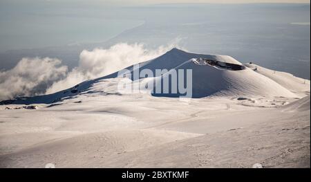 Cratere del vulcano Etna nel paesaggio innevato con nuvole e il golfo di Catania da sfondo Stockfoto