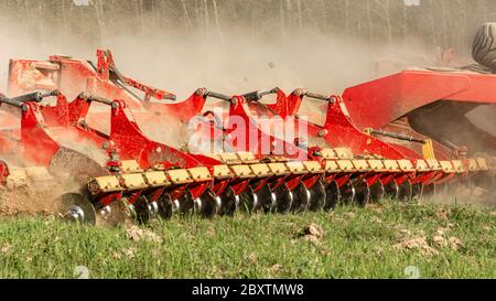 Die landwirtschaftliche Ausrüstung zerschneidet das gepflügte Land. Ein Raupentraktor zieht eine Egge, um den Boden aus nächster Nähe zu lockern. Stockfoto