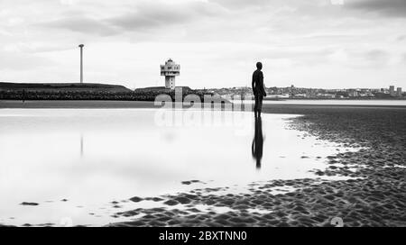 Einer der hundert Iron Men (von Antony Gormley geschaffen), der im Juni 2020 an der Küste von Crosby (bei Liverpool) neben einem Leuchtturm gefangen genommen wurde. Stockfoto