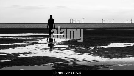 Einer der hundert Iron Men (von Antony Gormley geschaffen), der im Juni 2020 von der Crosby-Küste aus auf einen Windpark in der Irischen See blickte Stockfoto