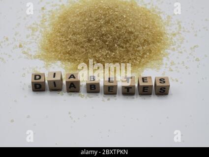 Nahaufnahme von isolierten Pfahlbraunen Zuckerkristallen, weißer Hintergrund. Wort Diabetes buchstabiert mit hölzernen Buchstaben Fliesen. Stockfoto