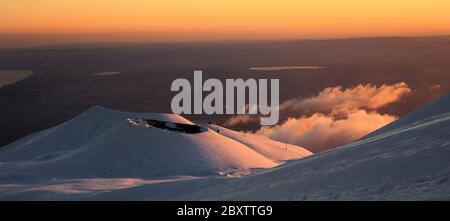 Cratere del vulcano Etna nel paesaggio innevato con nuvole e il golfo di Catania da sfondo al tramonto Stockfoto