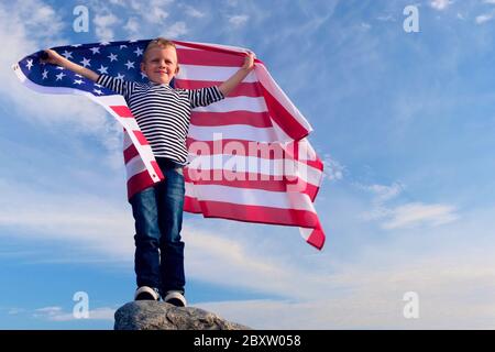 4k. Blonde Junge winkt nationale USA-Flagge im Freien über blauen Himmel im Sommer - amerikanische Flagge, Land, Patriotismus, Unabhängigkeitstag 4. juli. Stockfoto
