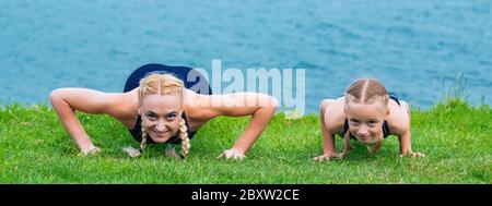 Kleine Girte und Frau machen Übungen auf dem Gras am Ufer des Sees. Stockfoto