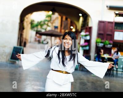 Lateinische Brünette Frau in weiß gekleidet lachen Blick auf die Kamera mit ausgestreckten Armen. Lifestyle-Konzept Stockfoto