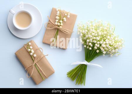 Flache Lage Zusammensetzung mit Kaffeetasse, zwei Geschenkboxen verpackt Bastelpapier, Blumen Lilie des Tals auf blauen Tisch Ansicht. Romantisches Frühstück Stockfoto