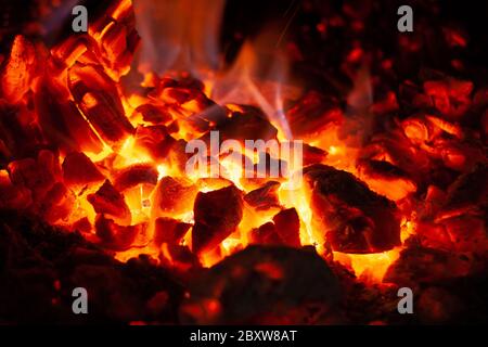 Glühende Glut in glühender roter Farbe, abstrakter Hintergrund. Die heiße Glut brennenden Holzes logs Feuer. Brennholz auf dem Grill. Textur von Feuer Brennstoff Briquet Stockfoto