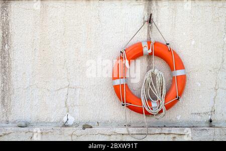 Die Rettungsboje mit Kordel ist auf Betonwand Hintergrund in der Nähe des Strandes aufgehängt Stockfoto