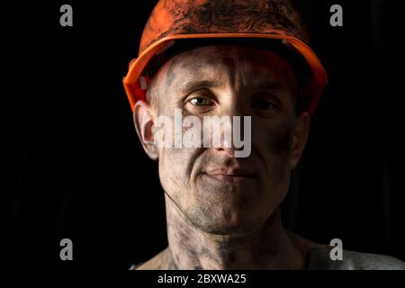 Das Gesicht eines männlichen Bergarbeiters in einem Helm auf schwarzem Hintergrund. Stockfoto