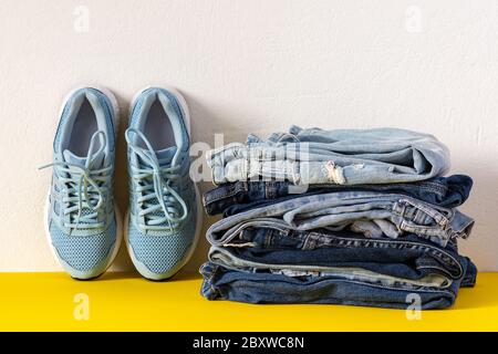Ein Stapel von verschiedenen Jeans Hosen und blauen Sneakers schließen auf gelb und weiß Hintergrund, lässige Kleidung, Sport-Stil Stockfoto