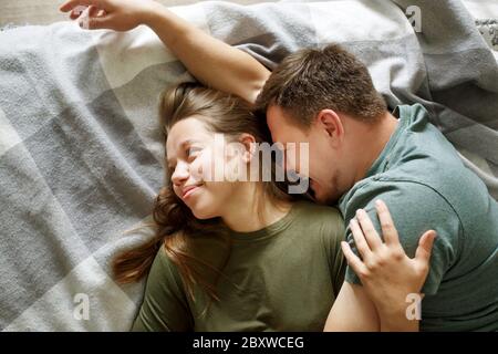 Portrait von lächelnd liebenden Paar auf einem Bett zusammen liegend, bleiben zu Hause Konzept, Draufsicht. Junge Freund und Freundin umarmen, echte Menschen. Stockfoto