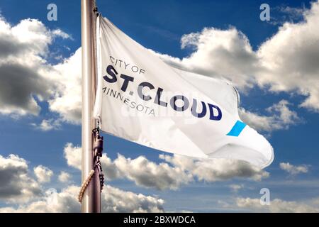 Das City of St. Cloud, Minnesota Logo auf einer weißen Flagge hisste einen Fahnenmast mit blauem Himmel und geschwollenen weißen Wolken in St. Cloud, MN, USA Stockfoto