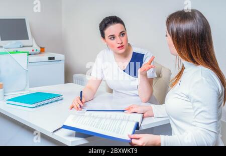 Junge Ärztin sitzt an ihrem Schreibtisch und plaudert mit der Patientin, während sie ihre Testergebnisse zeigt Stockfoto