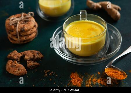 Tasse Ayurveda-Getränk goldene Milch Kurkuma Latte mit Curcuma Pulver, Ingwer und Honig über grüne Textur Hintergrund. Stockfoto