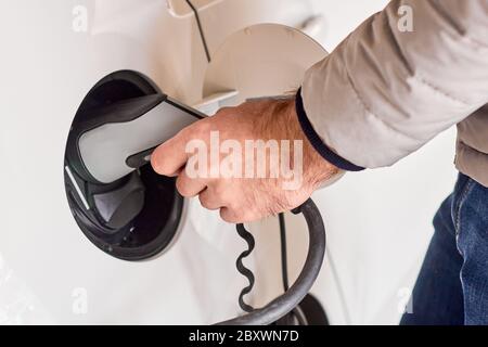 Nahaufnahme mans Hand hält ein Ladegerät Stecker eines Elektroautos. Umweltfreundliches Stadtfahrzeug. Stockfoto
