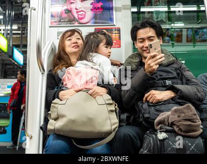 Eltern mit ihrem kleinen Kleinkind fahren mit dem Zug nach Hause und unterhalten das Kind mit ihrem Smartphone in Tokio, Japan. Stockfoto