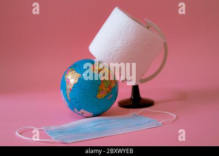 Erdkugel, Toilettenpapier und Gesichtsmaske auf rosa Hintergrund Stockfoto