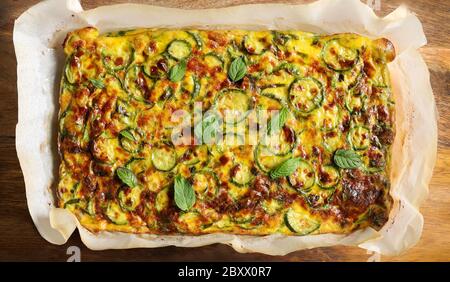 Gesundes Essen Konzept. Köstliche Omelette mit Zucchini und Lauch im Ofen auf Holzhintergrund gebacken. Vegetarisches Essen. Dekoration aus minzgrünen Blättern. Draufsicht Stockfoto
