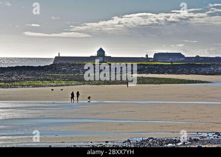 Ein Blick über Sandy Bay, Porthcawl, bei Ebbe. Wellenbrecher & Leuchtturm in der Ferne.Menschen auf Sand spazieren. Stockfoto