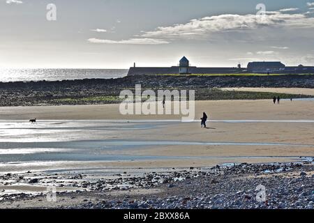 Ein Blick über Sandy Bay, Porthcawl, bei Ebbe. Wellenbrecher & Leuchtturm in der Ferne.Menschen auf Sand spazieren. Stockfoto