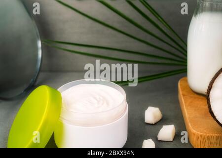 Nahaufnahme geöffnete Creme für Körperpflege mit Kokosöl, frischen Kokosnüssen, Palmblatt, Flasche mit Kokosbutter und Spiegel auf dunkelgrauem Hintergrund. Entfällt Stockfoto