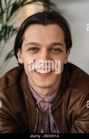 Porträt eines erfolgreichen jungen Mannes mit glücklicher emotionaler Gesichts posiert für Bilder. Positiver Hipster trägt lässige Kleidung lachend, sitzt im Café Stockfoto