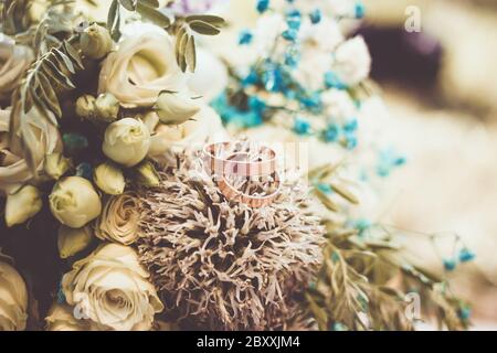 Nahaufnahme der Hochzeitsringe auf rustikalem Blumenstrauß Stockfoto