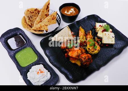 tandoori-Platte mit Hühnchen-Tikka, gegrillten Garnelen und Paneer zusammen mit Dal Makhani, Weizenbrot und Chutneys, indische Spezialität Stockfoto