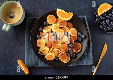 Blick von oben auf hausgemachte Mini-Pfannkuchen auf einem schwarzen Teller Auf blauem Hintergrund Stockfoto