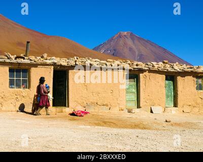 Grundhaus aus Adobes und bolivianischer Frau in typischem Kleid. Licancabur Vulkan im Hintergrund, Altiplano, Bolivien. Stockfoto