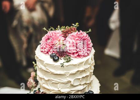 Nahaufnahme von weißen Hochzeitstorte von rosa Dahlia Blumen Hochzeit Partei im Hintergrund dekoriert. Konzept für Hochzeitstag. Stockfoto