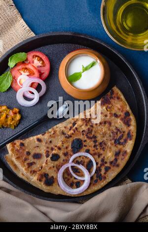 Aloo Paratha / Indische Kartoffel gefülltes Weizenbrot serviert mit Quark & Pickle, Tomaten & Zwiebeln. Draufsicht auf einem dunklen Moody Hintergrund. Traditionell Nord Ind Stockfoto