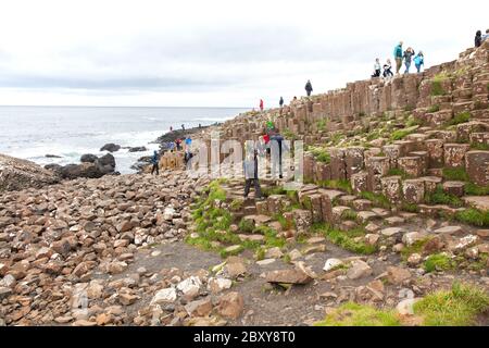 Menschen, die die Tausenden von alten ineinandergreifenden Basaltsäulen des Giant's Causeway an der Nordküste der Grafschaft Antrim, Nordirland, erkunden. Stockfoto