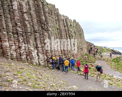 Menschen, die die Tausenden von alten ineinandergreifenden Basaltsäulen des Giant's Causeway an der Nordküste der Grafschaft Antrim, Nordirland, erkunden. Stockfoto