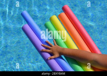 Frauenarm hält Poolnudeln in einer Regenbogenfarbsequenz in einem Schwimmbad zur Unterstützung von LGBTQ Pride Stockfoto