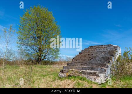 Eine alte Reihe von führt bis ins nichts. Die Treppen bröckeln stellenweise und haben Moos und Flechten auf ihnen. Baum im Hintergrund, blauer Himmel oben. Stockfoto