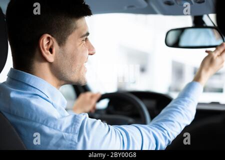 Kerl, der den Rareview-Spiegel im Fahrersitz überprüft Stockfoto