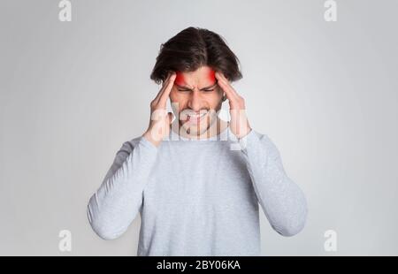 Kopfschmerzen in Schläfen. Mann mit Gesichtsausdruck in Schmerzen, drückt die Hände auf seinen Kopf mit roter Markierung, Studioaufnahme Stockfoto