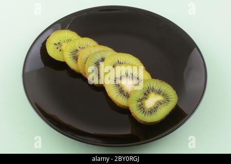 Rohe frische Kiwi-Fruchtscheiben auf schwarzem Teller auf hellgrünem Hintergrund Stockfoto