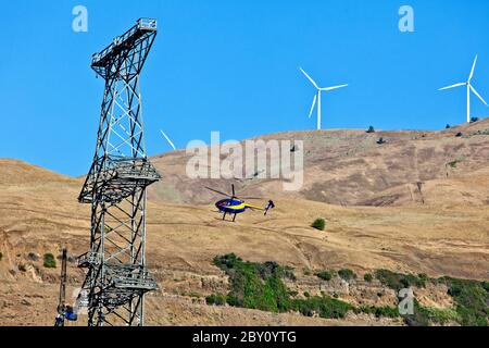 Hubschrauber transportiert Teile/Material zur Arbeitsmannschaft auf dem neuen Turm, elektrische Getriebe Turm. Hughes 500 Hubschrauber, Windpark im Hintergrund. Stockfoto